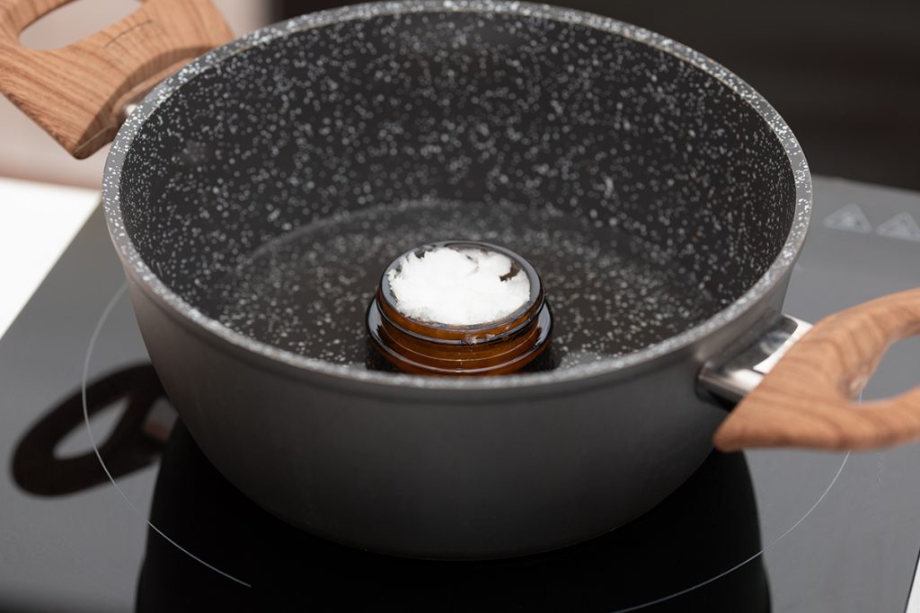 Foto einer mit festem Kokosöl gefüllten Cremedose im Wasserbad