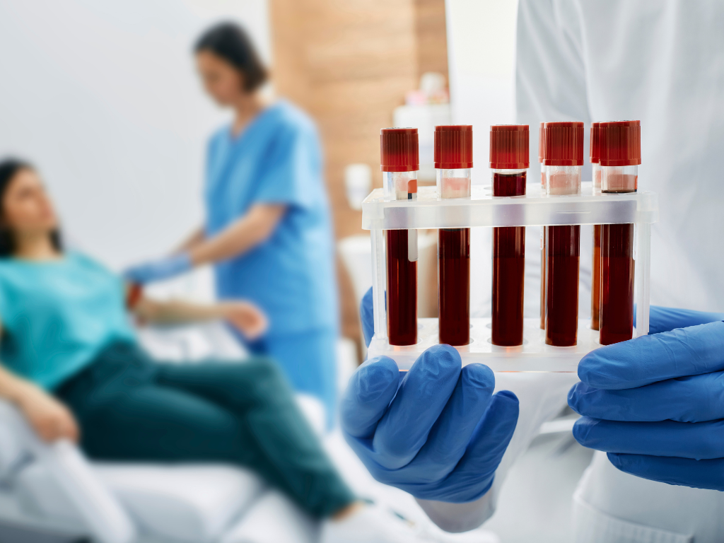 Schwester nimmt Patientin Blut ab, im Vordergrund mehrere mit Blut befüllte Röhrchen