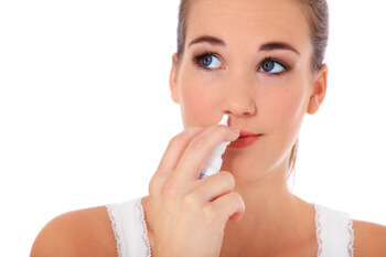 Frau befeuchtet die trockene Nasenschleimhaut mit einem Nasenpflegespray. 