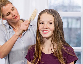 Für die Anwendung des NYDA® Läusekamms kämmt eine Mutter ihrer Tochter die Haare.