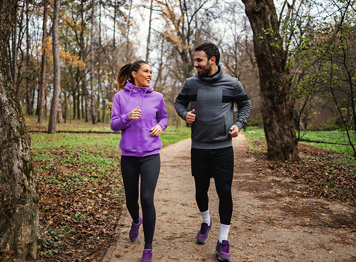 Eine Frau und ein Mann joggen fröhlich in einem Park.